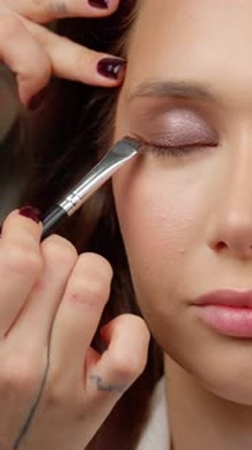 Makeup Professional trägt zarten rosa Lidschatten auf das Augenlid des Models auf, der zarte Schönheit zur Geltung bringt