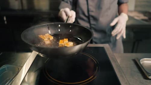 professional restaurant kitchen chef frying tofu cheese in a pan with oil tossing it asian cuisine