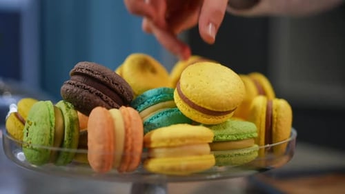 Hand places colorful macaron on cake stand