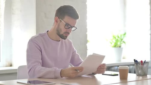 Young Man Reading Reports While Sitting in Office