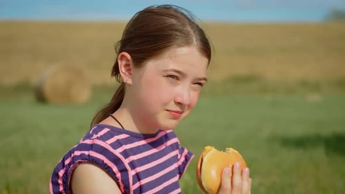 Girl Enjoys Eating a Hamburger in Rural Field