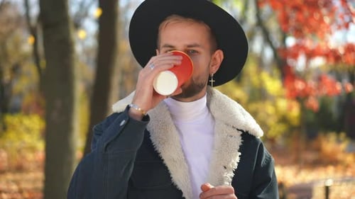 Front View Portrait of Handsome Caucasian Young Man Looking at Camera Drinking Coffee From