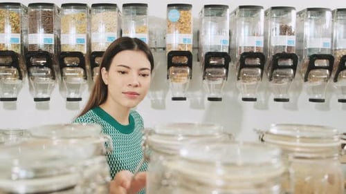 A young woman is shopping in refill store with reusable bag, zero-waste grocery.