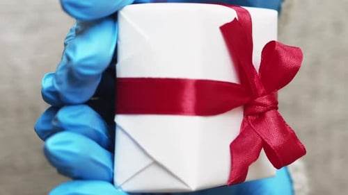 Gift Held by Hands Wearing Blue Medical Gloves