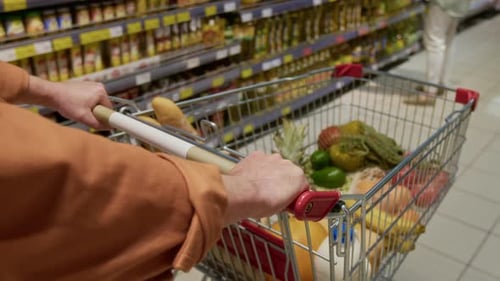 Unrecognisable Man Pushing Shopping Cart Filled with Groceries in Supermarket
