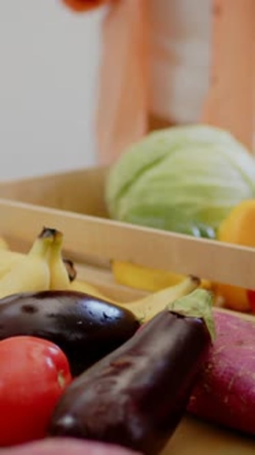 Vidéo verticale : Placer le céleri en entrant dans la main, elle range une caisse sur le dessus orange au comptoir