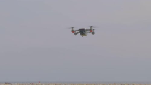 A closeup view of a flying drone camera, blinking lights and turning at the beach.