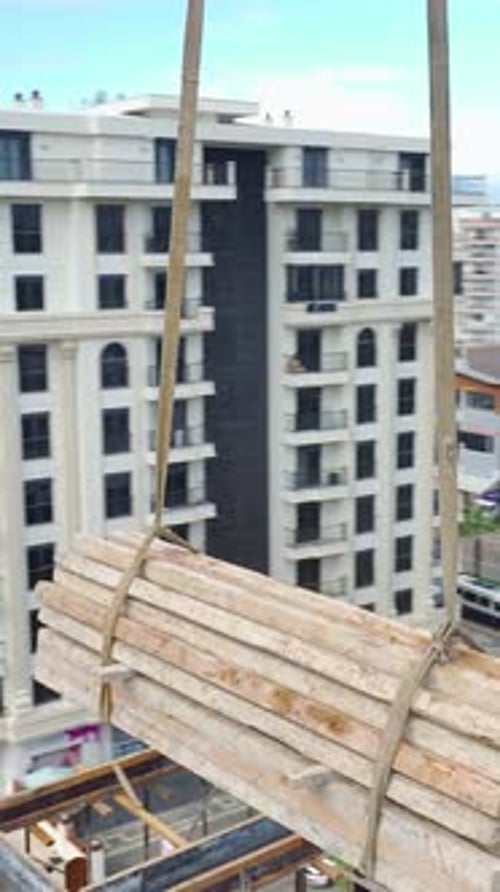 Vídeo vertical Los materiales de construcción pesados son levantados por grúas mientras los trabajadores gestionan las tareas in situ con