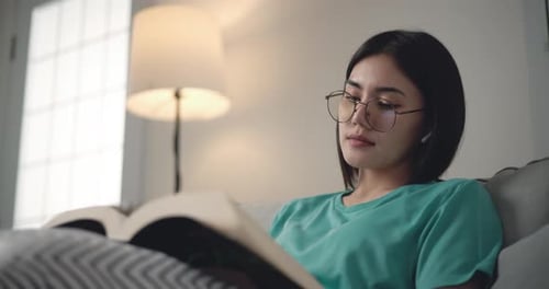 Woman Reading Book Reclining on Couch Indoors