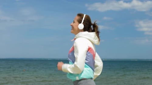 Smiling woman with headphones enjoying a morning run along a beautiful beach