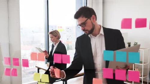 Profis, die mit Postit zusammenarbeiten, Notizen auf transparenter Bürotafel
