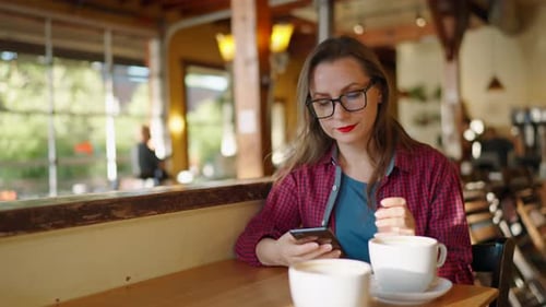 Woman is Using Smartphone and Drinking Coffee in the Cafe