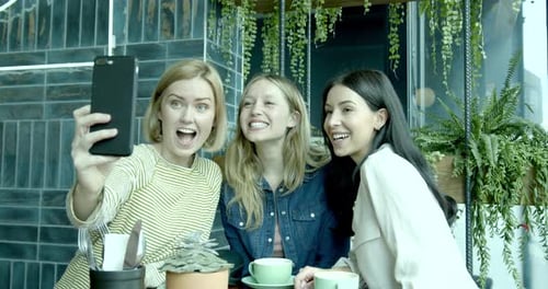Female Friends Taking selfie for social media on smart phone, having fun in Cafe.