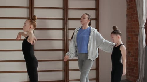 Teacher Walking between Two Flexible Girls and Helping Them Do New Exercises