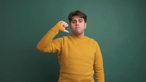 Upset Young Man Gesturing Thumb Down in Green Studio