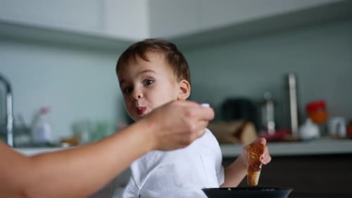 Adorável criança caucasiana sentada à mesa segurando um pedaço de pão.