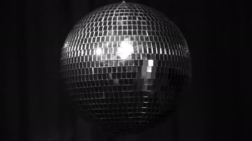 Shimmering silver disco ball rotating against a black backdrop