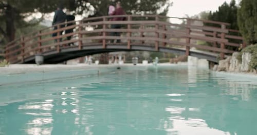 Clear Blue Water Pond in City Park and Families are Having Great Time by Walking on the Wooden Bridg