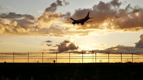 Passagierflugzeug landet bei Sonnenuntergang hinter dem Flughafenzaun