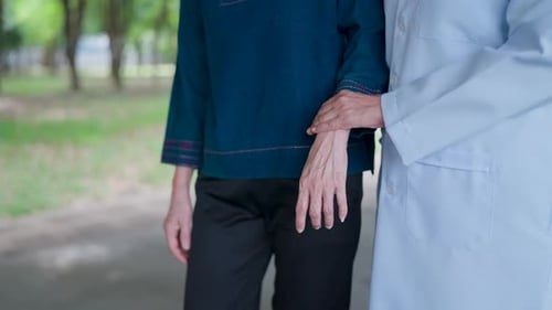 Close-up Asian nurse's hand supporting an elderly woman walking outside her home.