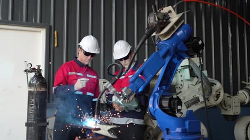 Multiracial engineers working with robot arm at robotic automation facility