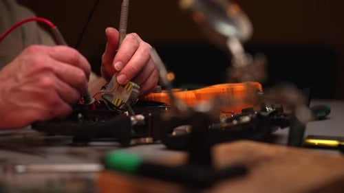 Nahaufnahme eines Technikers, der Bauteile auf die Leiterplatte einer zerlegten Fpv-Drohne lötet