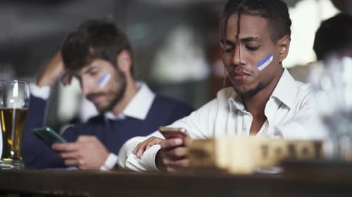 Football Fans are Sitting in a Bar During a Football Match and Using Their Smartphones Watching a