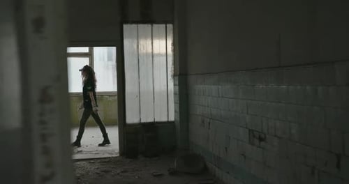 Einblicke in eine Frau in einem verlassenen Gebäude, als sie eine Passage entlang geht, die an offenen Türen vorbeiführt