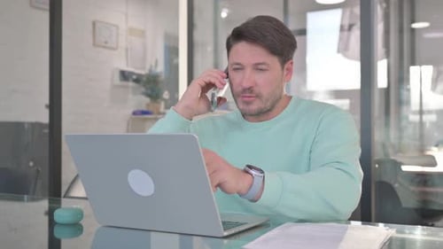 Man Talking on Phone While Using Laptop at Work