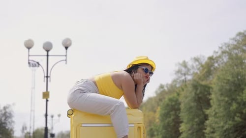 Young Woman Resting on Suitcase in Urban Park