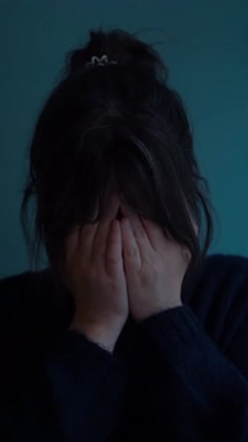 Distressed woman covering face in dimly lit room