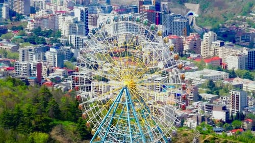 Drohnenaufnahme von Tiflis vom Mtatsminda-Hügel aus mit Riesenrad, Skyline der Stadt, Fluss und