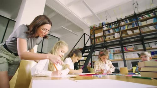 Elementary School Students Sit at a Round Table in an Art Class and a Young Modern Teacher in