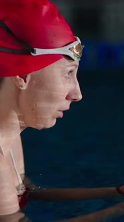 Focused Female Swimmer in Red Cap Preparing for Training in Indoor Pool Transitioning From Fatigue
