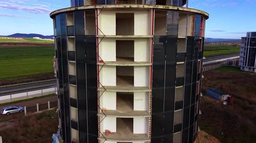 Construcción de un edificio de gran altura con forma de cilindro. El transporte viaja por la autopista como telón de fondo.