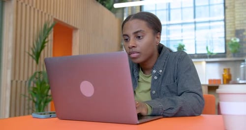 Femme d'affaires noire travaillant dans un bureau à aire ouverte sur un ordinateur portable