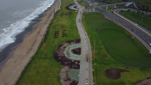 Parque verde cubierto de hierba con una larga pasarela junto a la orilla del mar a la izquierda y una autopista a la derecha. Dro