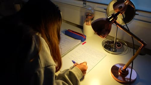 Girl studying at night, writing down the notes for classes