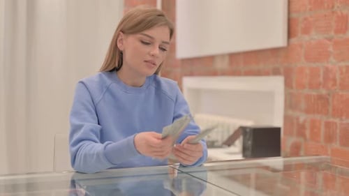 Young Woman Counting Dollar Bills at Table