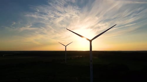 Large wind turbines with blades in field aerial view bright orange sunset blue sky wind park slow mo