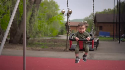 A Happy One Year Old Boy Swings on a Swing and Laughs Little Child on the Playground