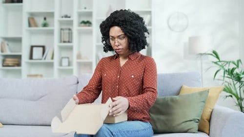 Woman Unboxes Small Package with Confused Expression