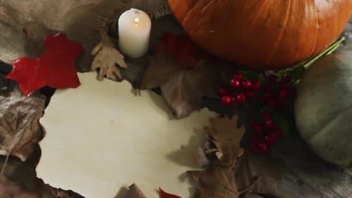 Paper with copy space against autumn leaves, candle and pumpkins on wooden surface