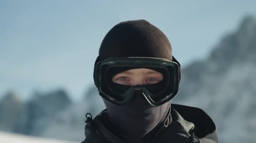 male putting on ski goggles in slowmotion with a mountain backdrop.