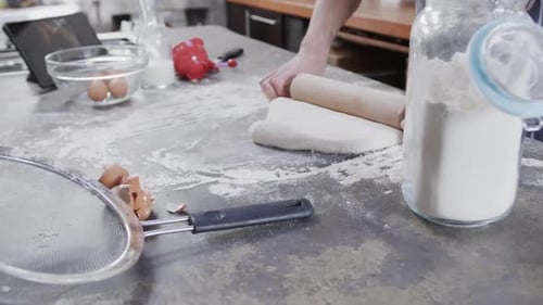 Hands of caucasian man preparing bread dough using tablet in kitchen, slow motion