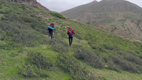 Two Hikers Walking Across Green Hillside Exploring Open Mountain Landscape Showing Freedom Adventure