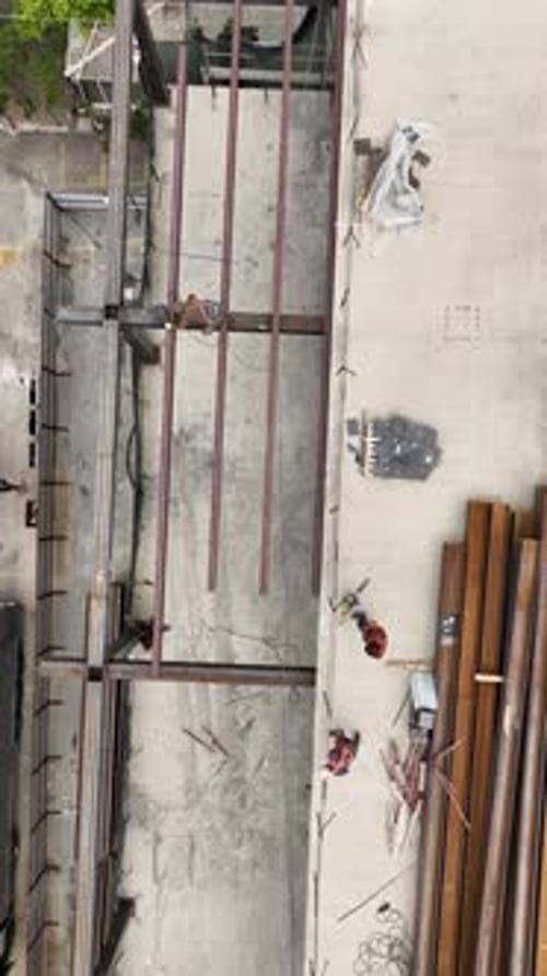 Vídeo vertical: toma aérea de trabajadores de la construcción de edificios descargando vigas de acero en un lugar prominente