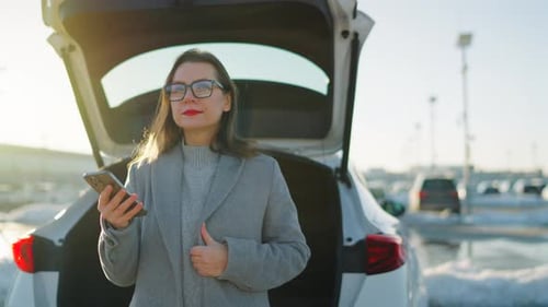 Woman Using Phone by Open Car Trunk on Sunny Day