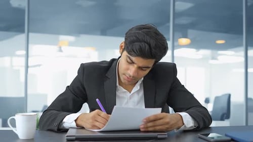 Young Adult Reviews Documents in Modern Office