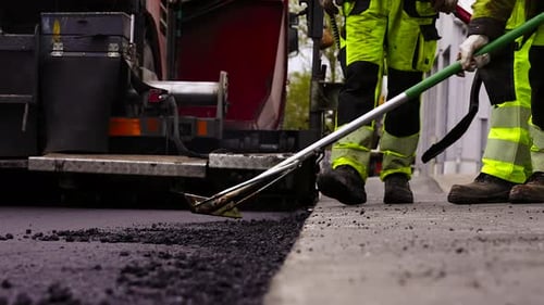 Worker Levels Asphalt Freshly Spread on Gravel with an Asphalt Screed.